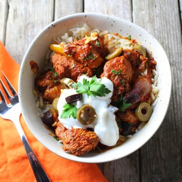 Bowl of marinaded harissa chicken cooked with onions and peppers with yogurt on top.