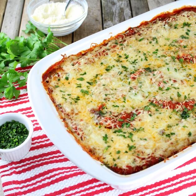 Partial casserole dish with cooked Lasagna topped with melted cheese and parsley