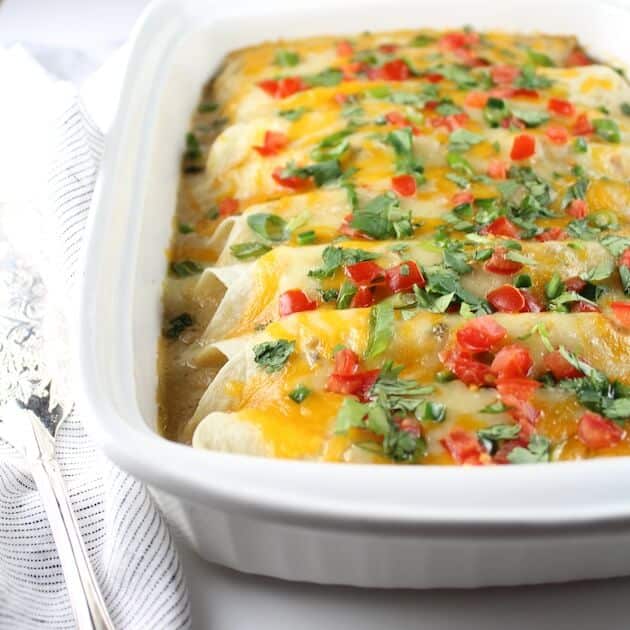 Partial Casserole dish of Chicken Enchiladas covered in cheese, tomatoes, and cilantro