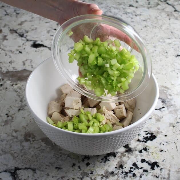 adding chopped celery to cubes of chicken in mixing bowl