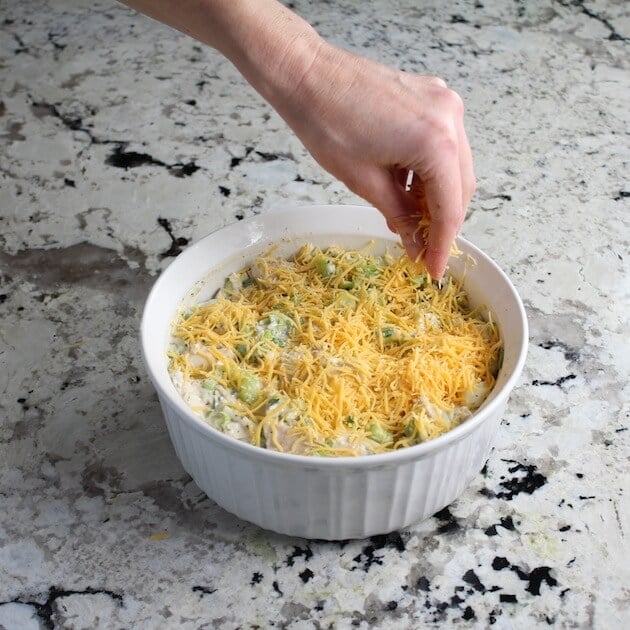 Adding shredded cheese to the top of chicken salad baking dish