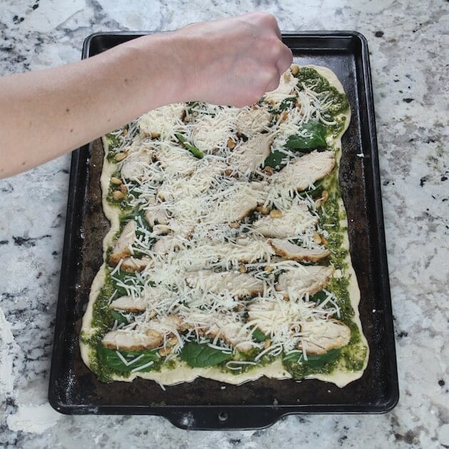 Adding shredded cheese to Chicken Pesto Pizza