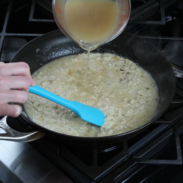 Adding chicken stock to creamy enchilada sauce cooking on stovetop