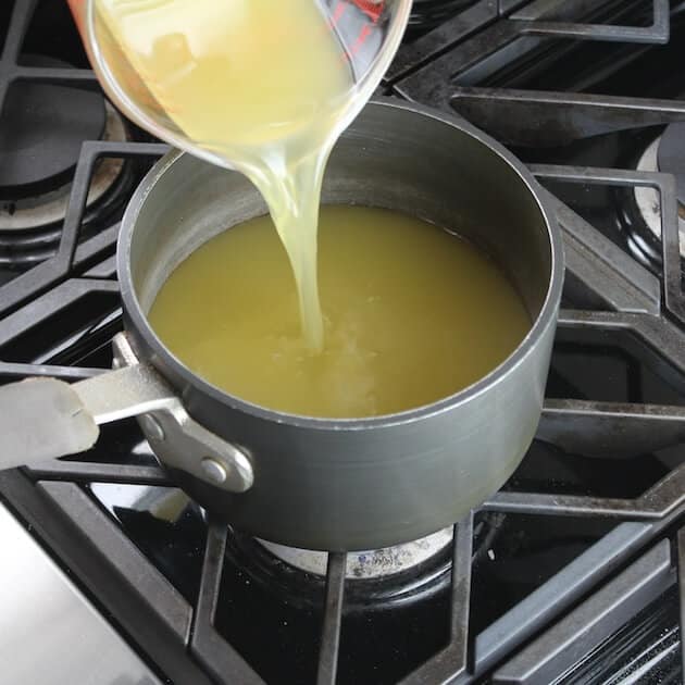 adding chicken stock to saucepan on stove