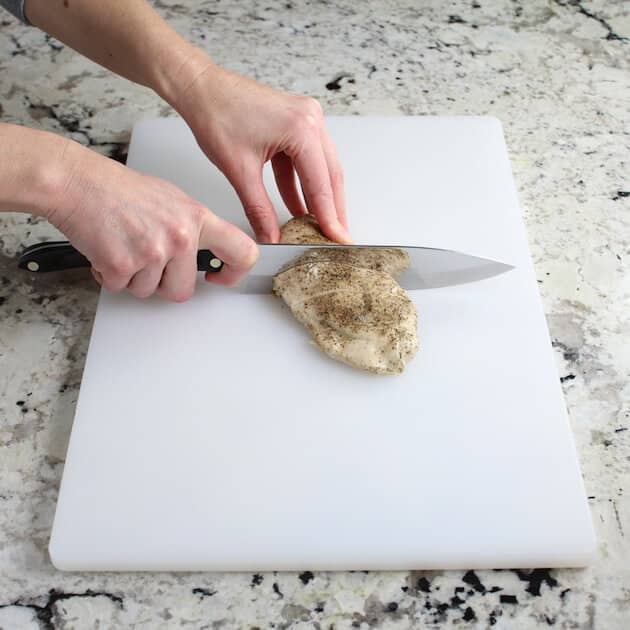 slicing cooked chicken breast on cutting board
