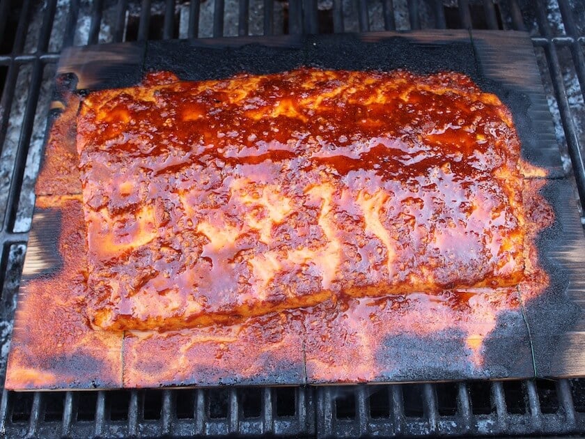 Side of Salmon on Cedar Plank Smoking on grill covered with Harissa marinade