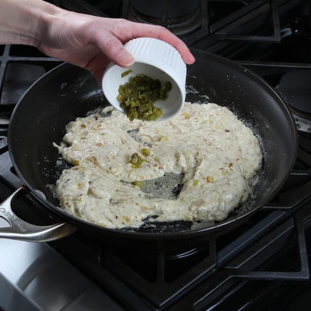 Adding diced jalapenos to sour cream mixture in saute pan