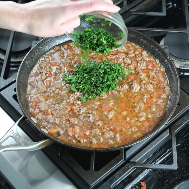 Adding parsley to saute pan of lasagna meat sauce