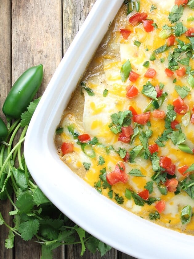 Partial Casserole dish of Chicken Enchiladas angled on farm table with cilantros