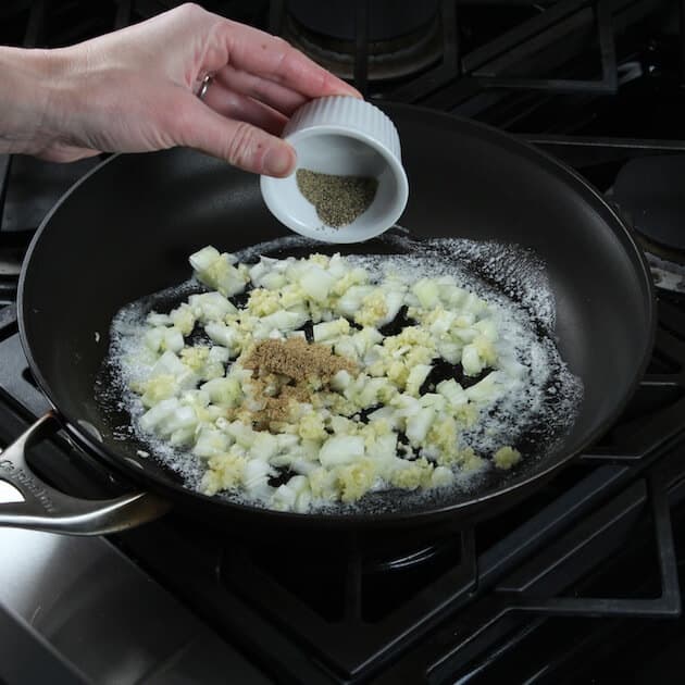 Adding pepper to saute pan with onions and garlic