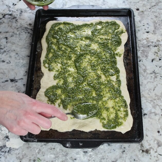 Adding pesto to pizza dough on baking sheet