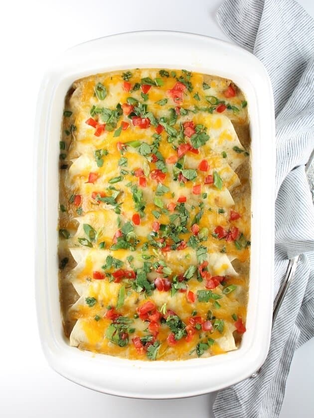 8 Cheesy Chicken Enchiladas in a white casserole dish with napkin