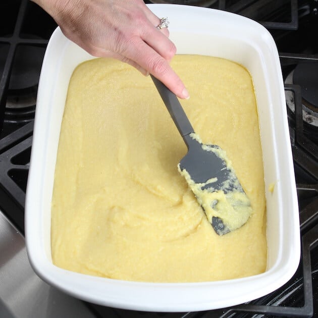 smoothing out polenta on bottom of a casserole dish