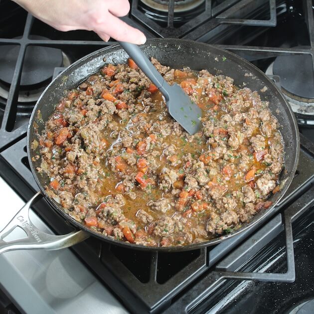 Stirring lamb lasagna meat mixture in saute pan
