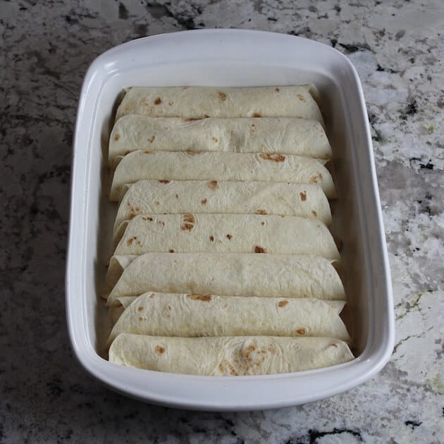 Stuffed tortillas lined up in casserole dish for enchiladas