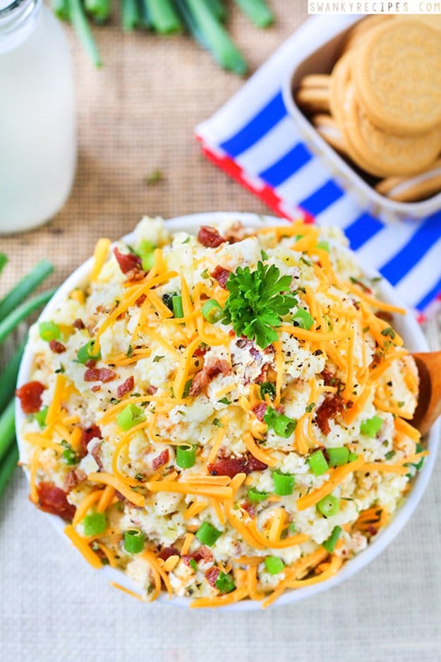 Bowl of potato salad topped with cheese, bacon, and onions