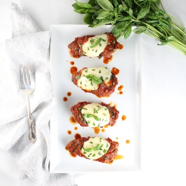 Four chicken breasts on a platter covered in marinara sauce with fresh mozzarella melted