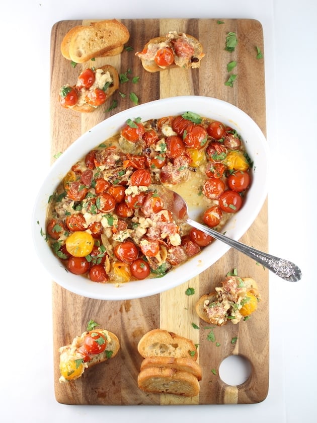 Yellow and red cherry tomatoes in dish on cutting board with slices of bread