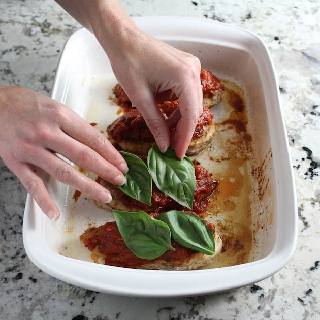 Adding basil to chicken breasts in casserole dish