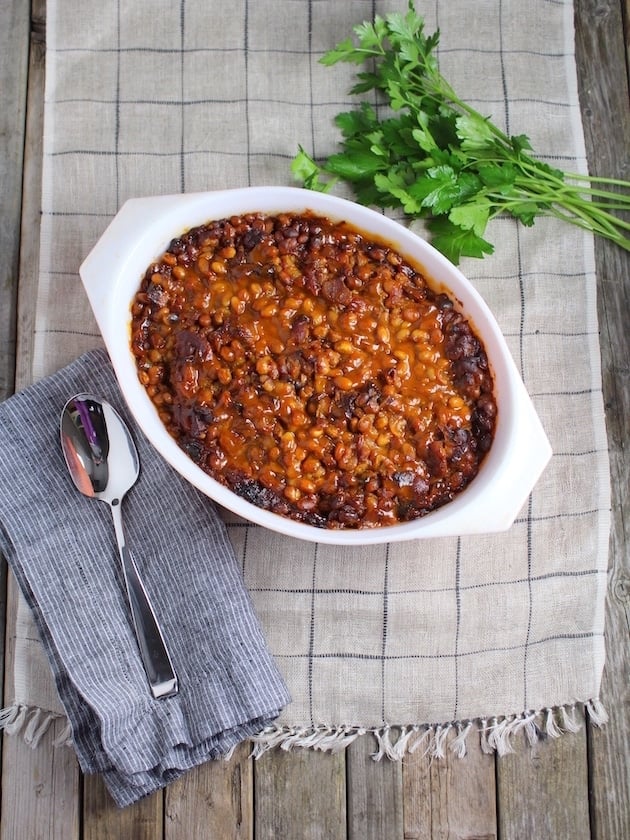 Farm table with a serving dish full of baked beans and sppon 