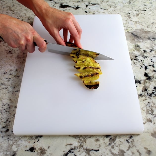 SLicing grilled yellow squash on cutting board