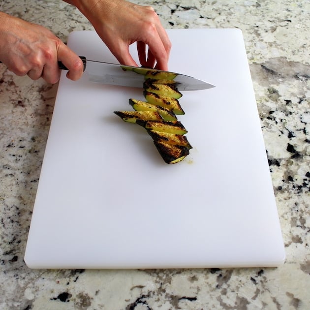 slicing grilled fresh zucchini on cutting board