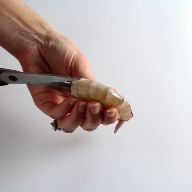 Using kitchen shears to remove shell from shrimp