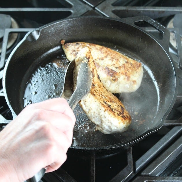 Turning over chicken seared in cast iron skillet