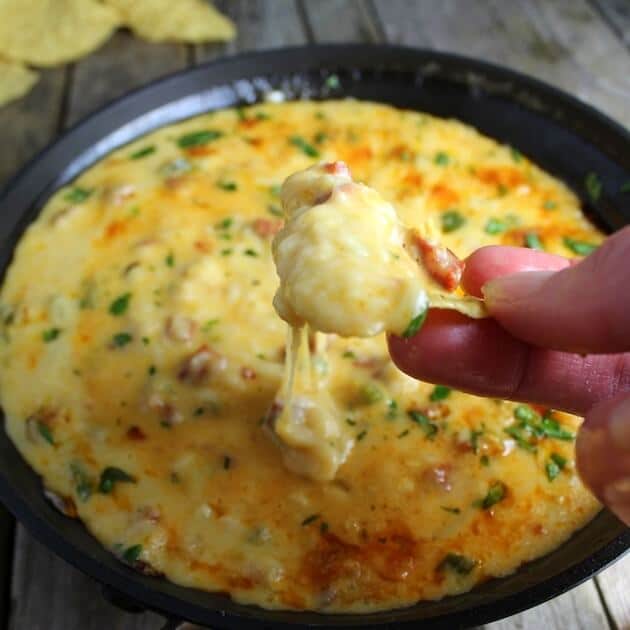 Hand dipping Corn chip into a skillet of Queso Fundido With Chorizo 