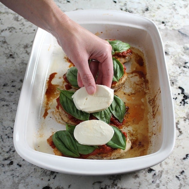 Adding fresh mozzarella to chicken caprese in baking dish