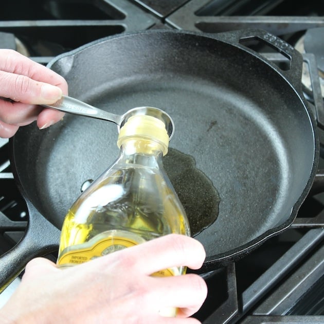 Adding olive oil to cast iron skillet on stovetop