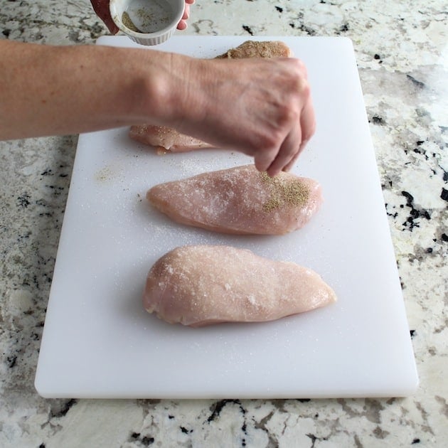 Adding pepper to chicken breasts on cutting board