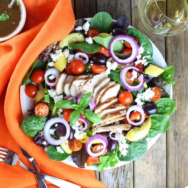 Grilled Mediterranean Chicken Salad on diner plate with silverware and glass of white wine