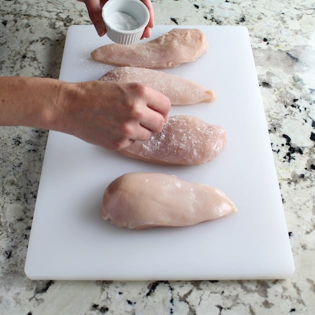 salting four boneless skinless chicken breasts on a cutting board