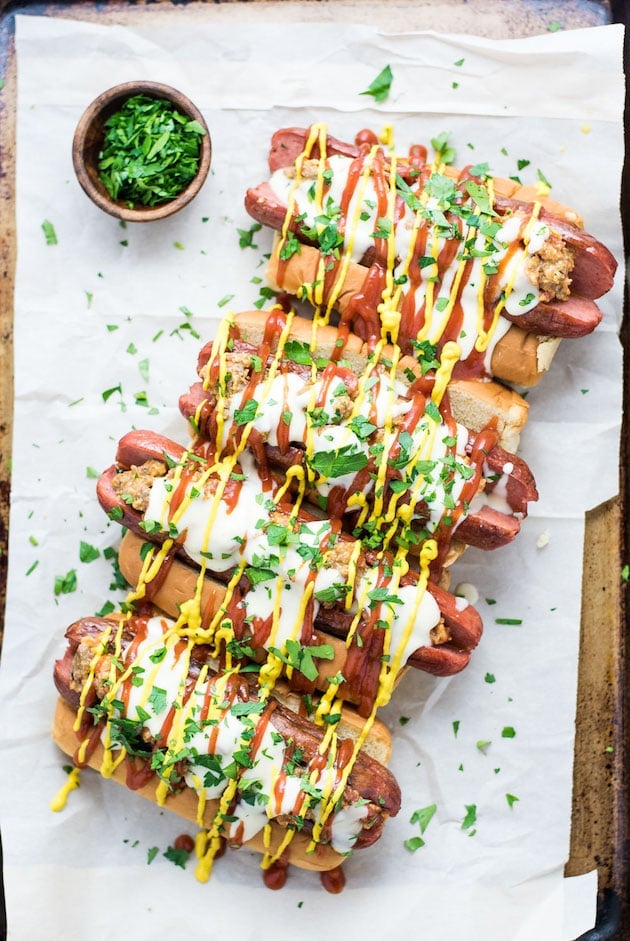 4 hot dogs lined up on parchment with mustard and ketchup on them 