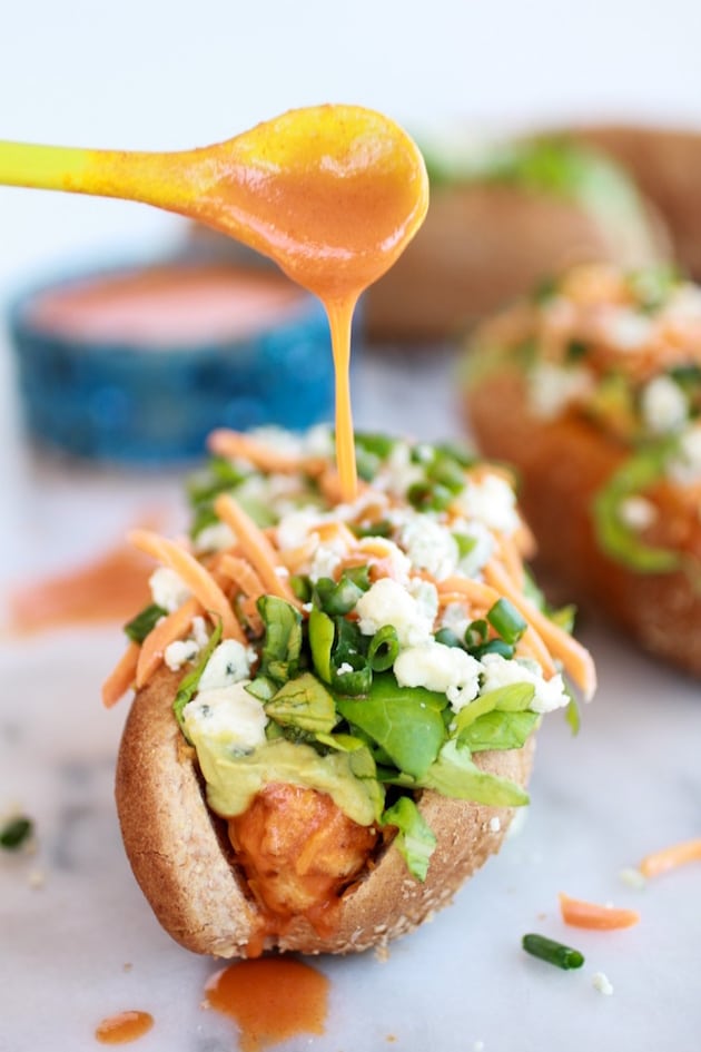 Spoon drizzling buffalo sauce on a buffalo Chicken hot Dogs