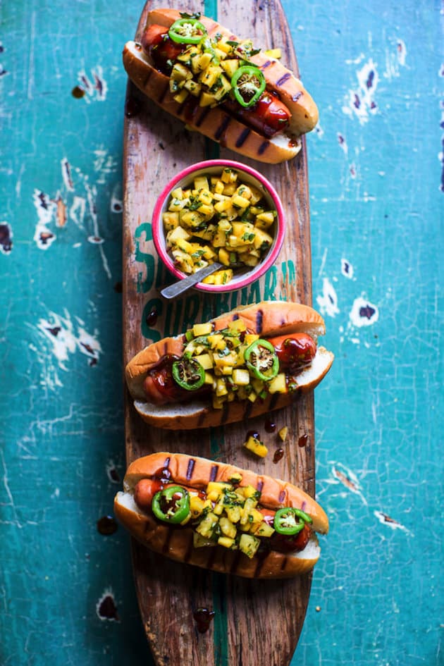 Three hot dogs with Hawaiian toppings on a wooden paddle 