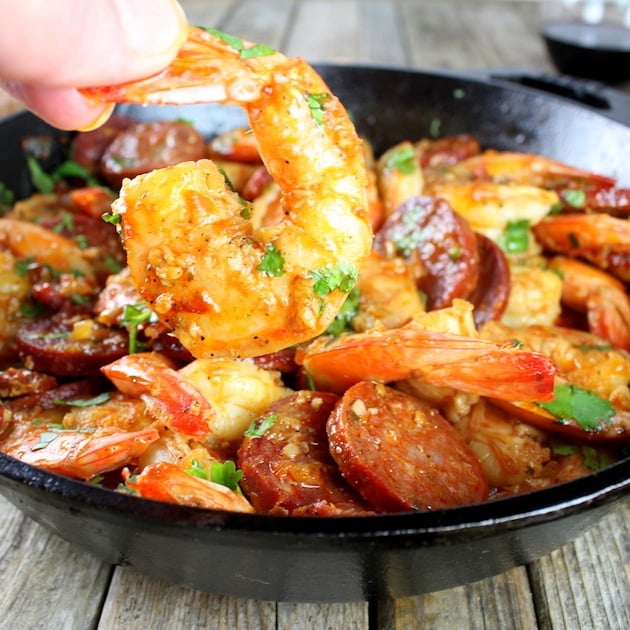 Hand holding shrimp in front of skillet of chorizo shrimp