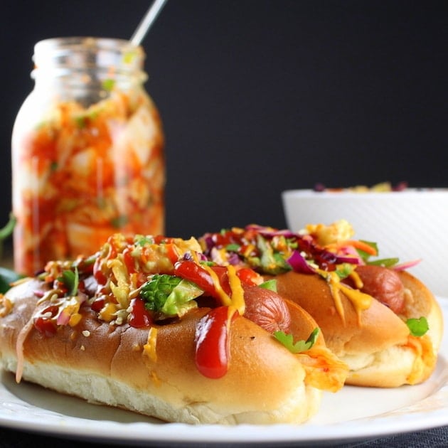 Two Korean Slaw Hot Dogs on plate with mason jar of Kimchi in background