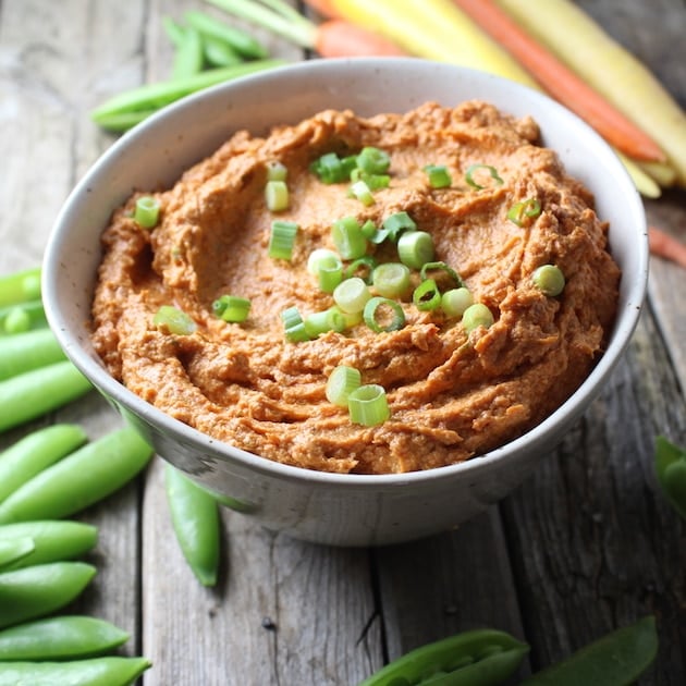 Sun-Dried Tomato Goat Cheese Dip in a serving bowl with surrounded by snap peas and carrots 