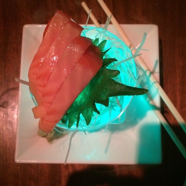 Sushi served on a neon lit glass dish with chopsticks