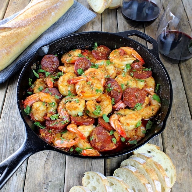 Cast iron skillet with shrimp chorizo appetizer on farm table with french bread 