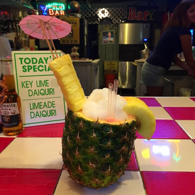 Huge tropical cocktail served in a pineapple with umbrellas and straws