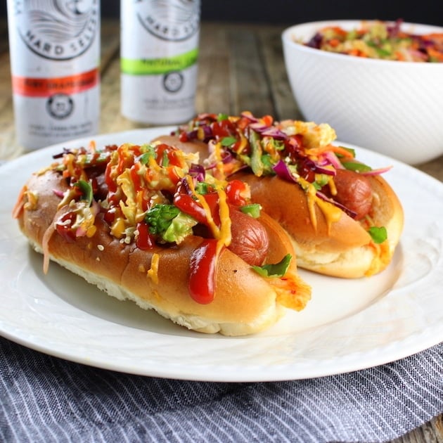 Two Korean Slaw Hot Dogs on plate with bowl of Asian slaw in background