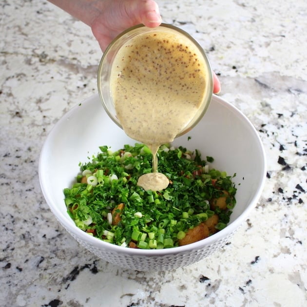 Adding mustard sauce to mixing bowl with potato salad