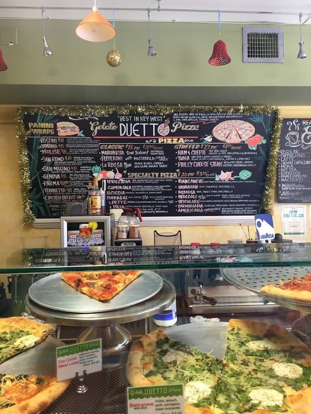 Pizzas in glass counter with fun menu in background at Duetto Pizza &amp; Gelato