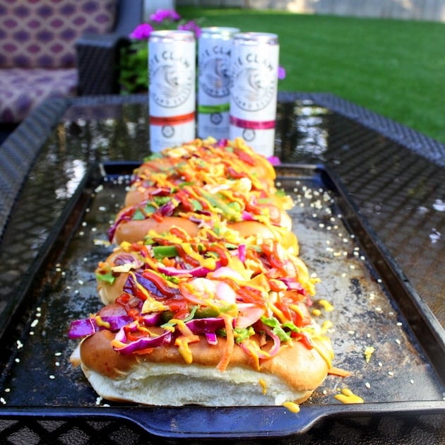 Five Korean Slaw Hot Dogs lined up on a cookie sheet on a backyard table