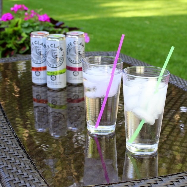 Glasses with ice and straws in backyard, with White Claw Hard Seltzer cans in background