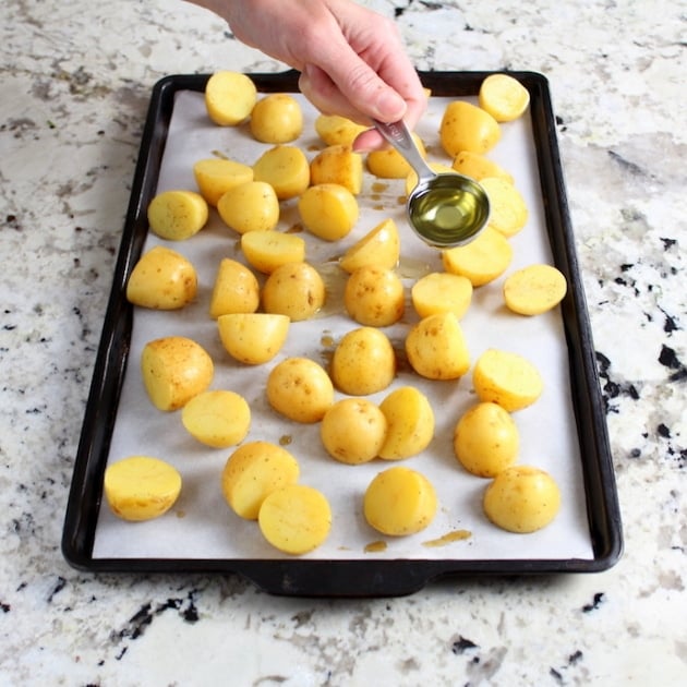 Adding olive oil to potatoes on baking sheet