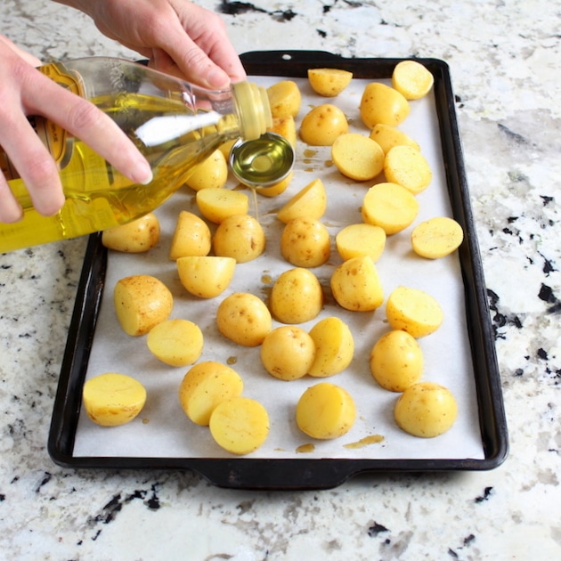 Adding olive oil to potatoes on baking sheet